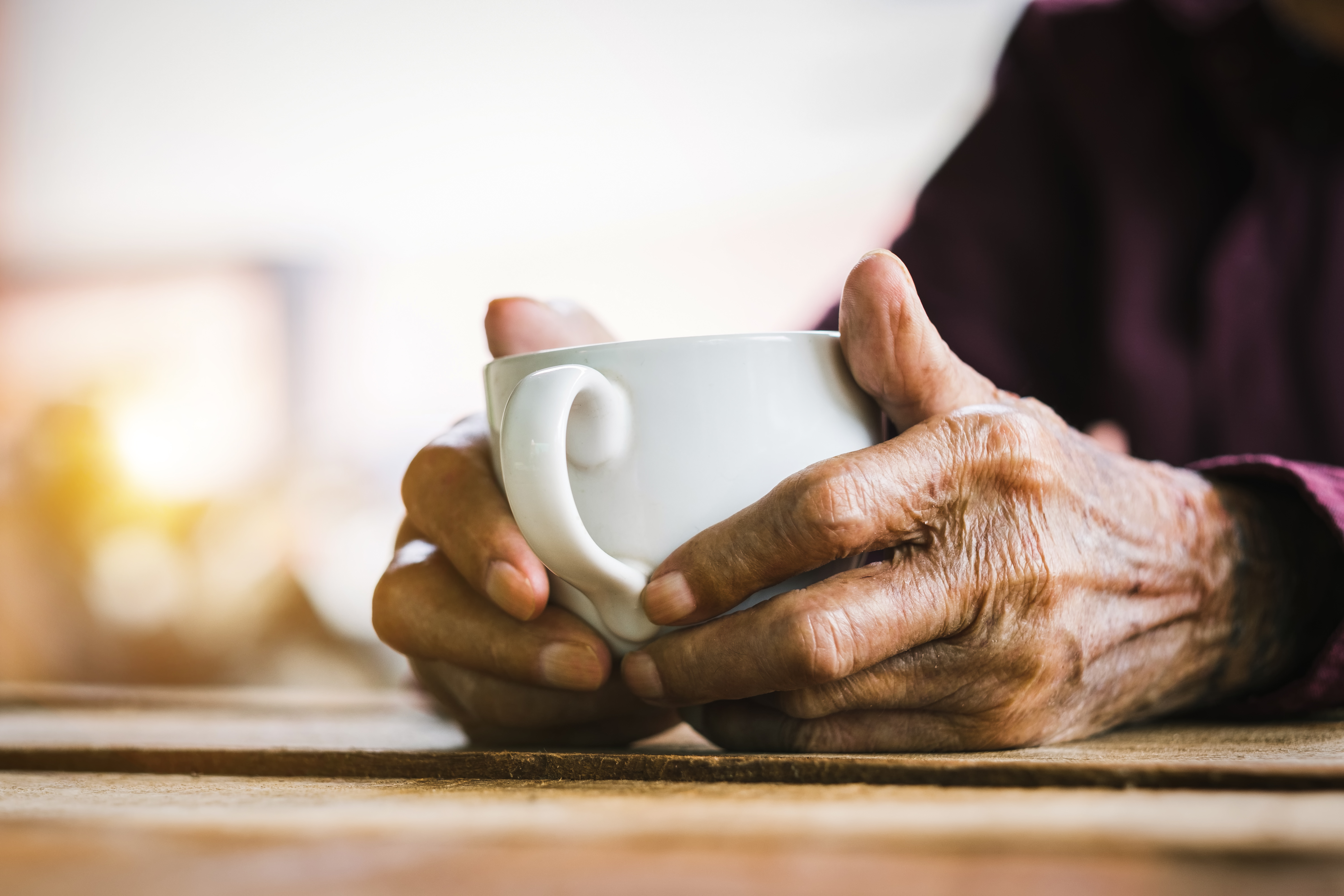 An older person holding a warm drink at home